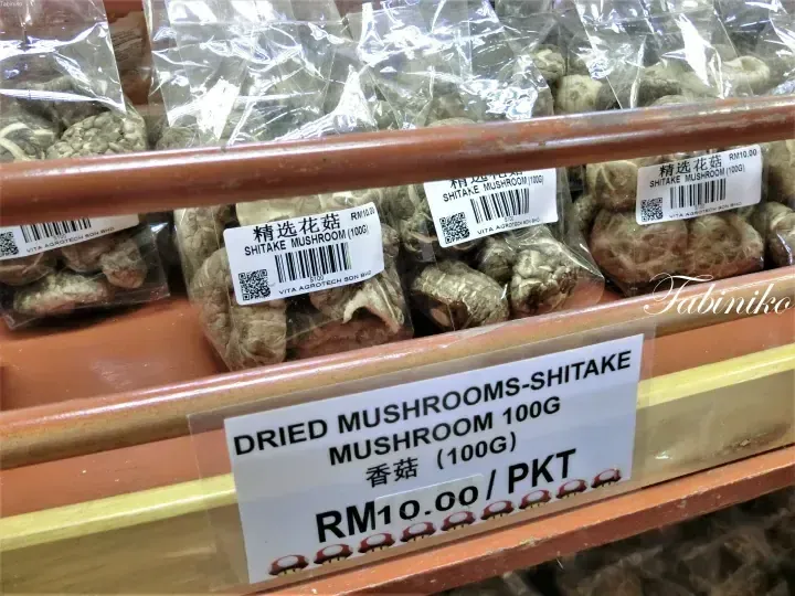 Shelves of dried shiitake mushrooms labeled in English and Chinese at a Malaysian grocery store.
