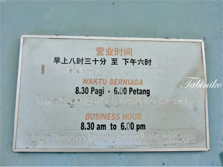 中国語、マレー語、英語で営業時間を記載した風化した看板。木曜日は休業。