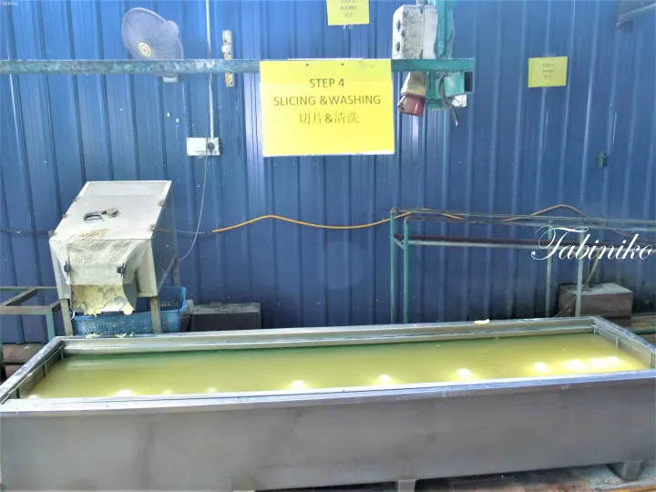 工場の大きな金属製洗浄槽の上に「STEP 4 SLICING & WASHING」と書かれた黄色い看板。