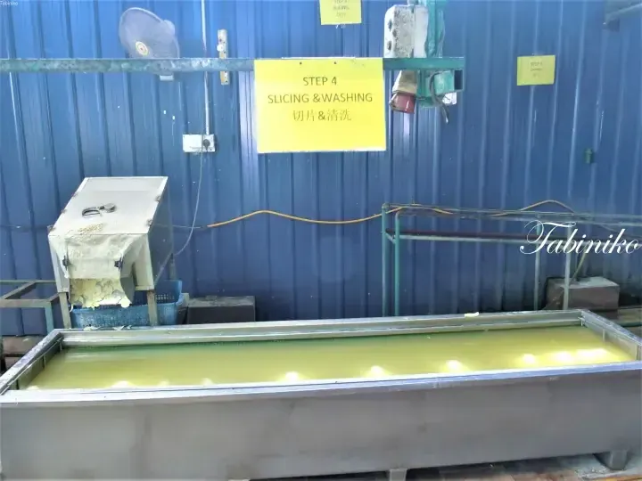 Yellow sign reading Step 4 Slicing & Washing above a large metal washing tank in a factory.
