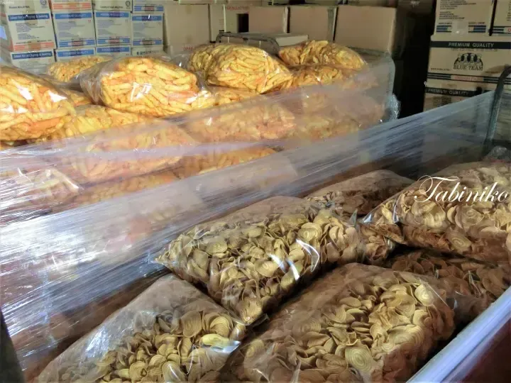 Large bags of yellow and brown spiral cookies displayed on shelves in a Malaysian bakery or snack shop.