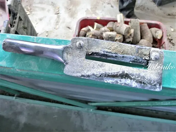 Close-up of a metal clamp on a green railing with a red container of firewood in the background