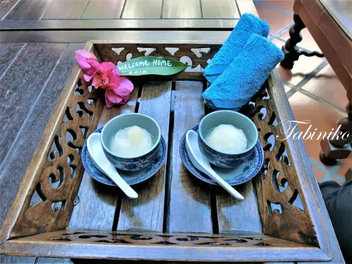 Welcome home refreshment tray with iced dessert, blue towel, and flower on wooden table at a Malaysian property.