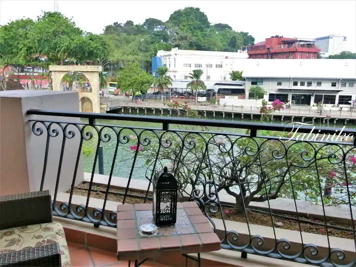 Balcony view of Melaka River with historic buildings and lush greenery in the background.