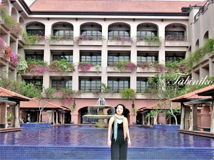A woman stands by a pool with a fountain at the courtyard of The Datai Langkawi resort, surrounded by balconies with vibrant bougainvillea.