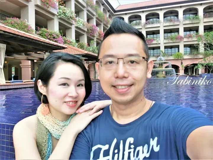 Couple smiling by the pool at The Datai Langkawi resort with its distinctive architecture and flower-filled balconies.