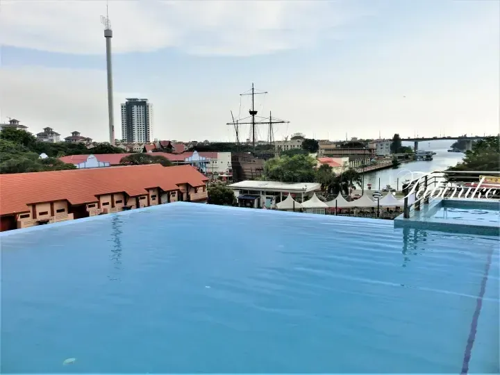 Infinity pool overlooking Melaka River, Dutch Square, and the Stadthuys with the Melaka Tower in the background.