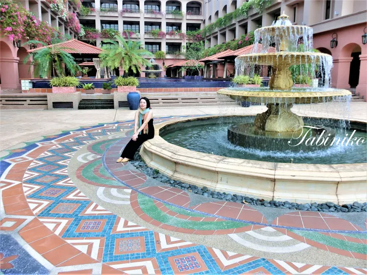 The Datai Langkawiの噴水のある中庭で、モザイクタイルと熱帯の緑に囲まれて座る女性。