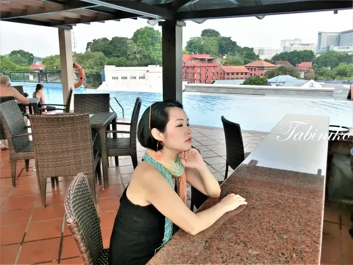 Woman relaxing at a poolside bar with a view of the red buildings and city skyline in Malacca, Malaysia.