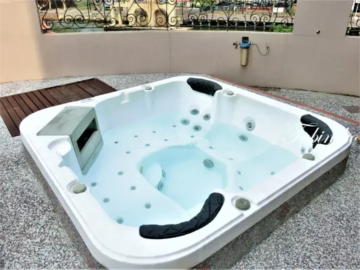 Outdoor jacuzzi tub with black cushions on a terrace overlooking a canal and stone bridge.
