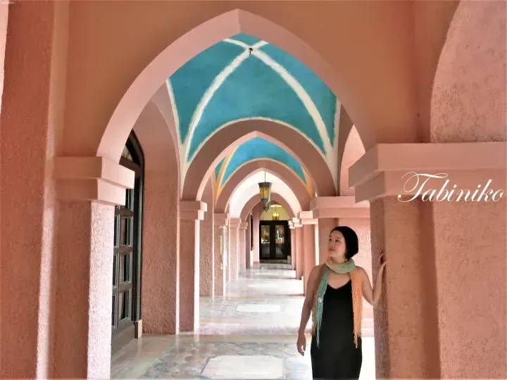 Woman standing in the pink arched corridor of The Datai Langkawi, featuring blue vaulted ceilings and tiled floors.
