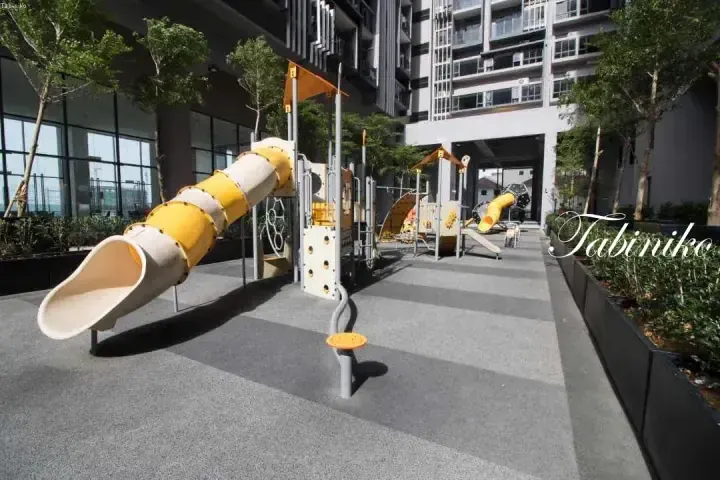 Modern playground with yellow and beige slides at a residential complex, featuring soft flooring and surrounding greenery.