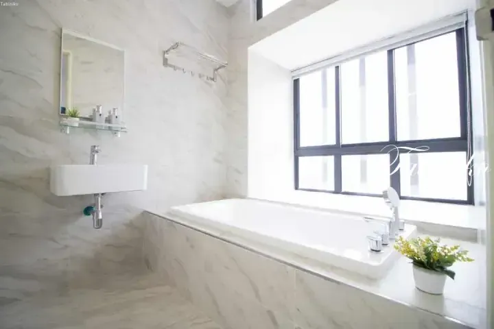 Modern bathroom with marble tiles, a white bathtub under a large window, and a wall-mounted sink.