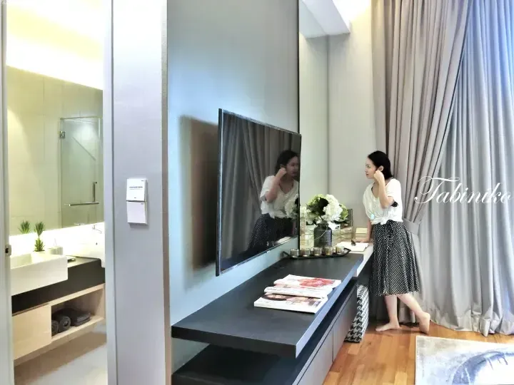 Woman adjusting earrings in a modern hotel room mirror near a vanity with flowers and magazines.