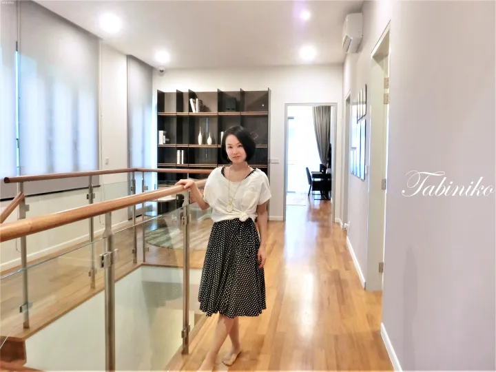 ガラス手すりと木製床のメザニンに立つ女性。背景にはモダンな家具が配置された室内が見える。