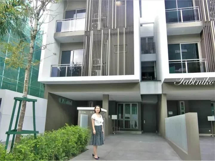 A woman stands in front of a modern apartment building entrance with vertical slat design and unit number B-23A.
