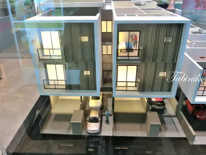 Architectural model of a modern two-storey terrace house with illuminated interiors, balconies, and ground floor parking.