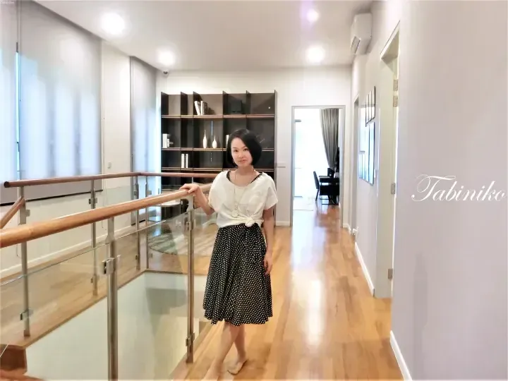 Woman in polka dot skirt standing on a wooden mezzanine with glass railing and built-in shelving in a modern home.