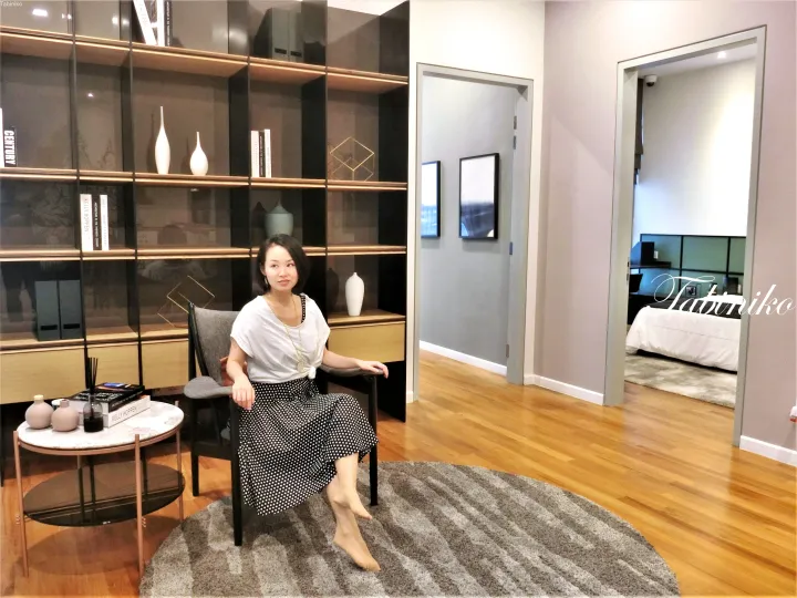 ガラスの書棚とベッドルームが見えるモダンなショールームに座る女性。