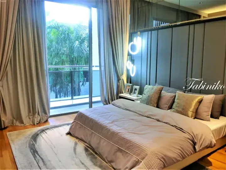 Modern bedroom with a large bed, grey curtains, and a balcony view of lush tropical greenery.