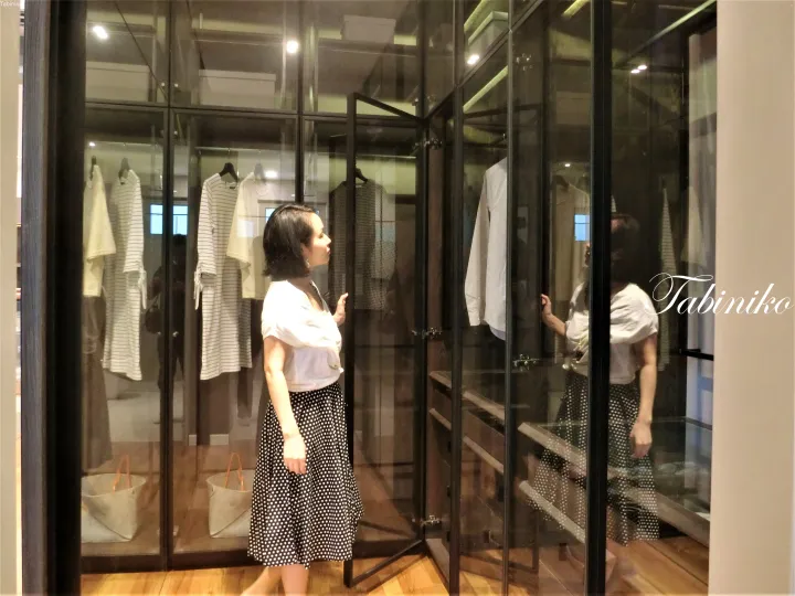 黒いフレームのガラス製ウォークインクローゼットで服を選ぶポルカドットスカートの女性。