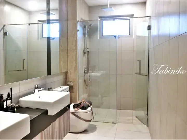 Modern bathroom with glass shower enclosure, white vessel sink, and beige tiles at Tabiniko