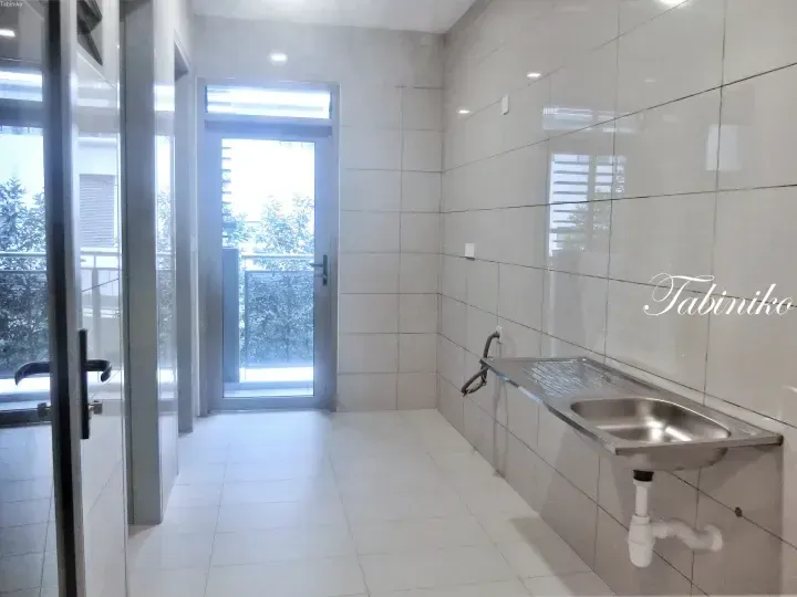 Modern laundry room with stainless steel sink, tiled walls, and glass door leading to a balcony with greenery.