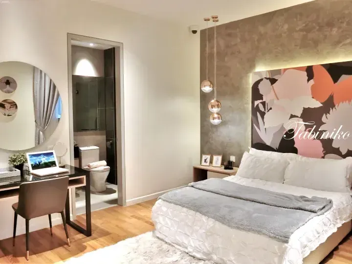 Modern hotel bedroom with floral wall art, pendant lights, and a vanity desk near the bathroom