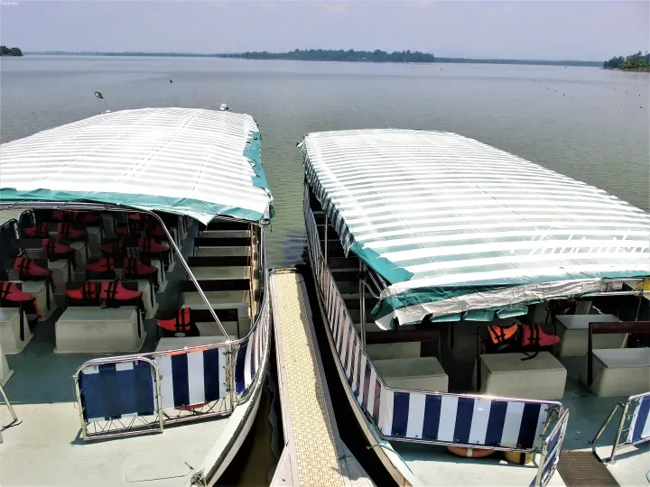 Two tour boats with striped canopies docked side-by-side at a jetty overlooking a wide river.