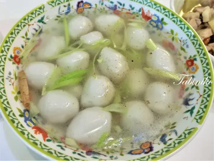 A bowl of white fish balls in clear soup with celery and pepper, served in a floral patterned bowl.