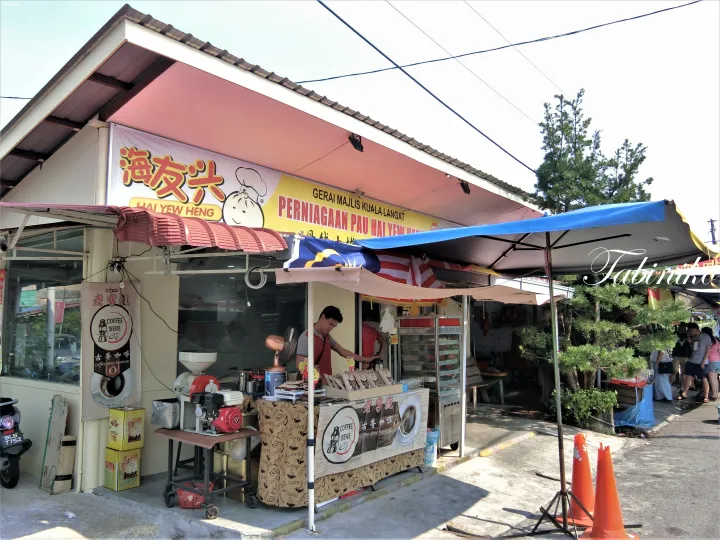 クアラランガットの「海友兴」店舗で、店員がカウンターで作業し、包子とコーヒーを販売している。