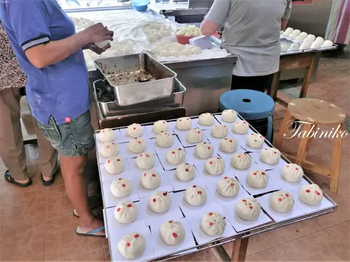 Workers preparing traditional Chinese buns with red dots on a wire rack in a Malaysian kitchen.
