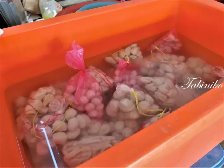 Orange tub filled with bags of fresh fish balls in water at a Malaysian market stall.
