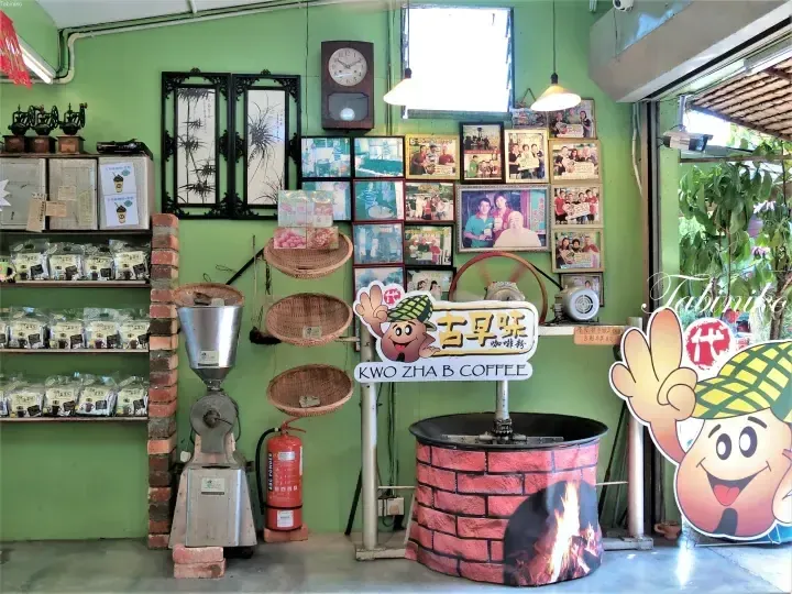 Interior of Kwo Zha B Coffee shop featuring a vintage coffee roaster, traditional baskets, and a green wall decorated with framed photos.
