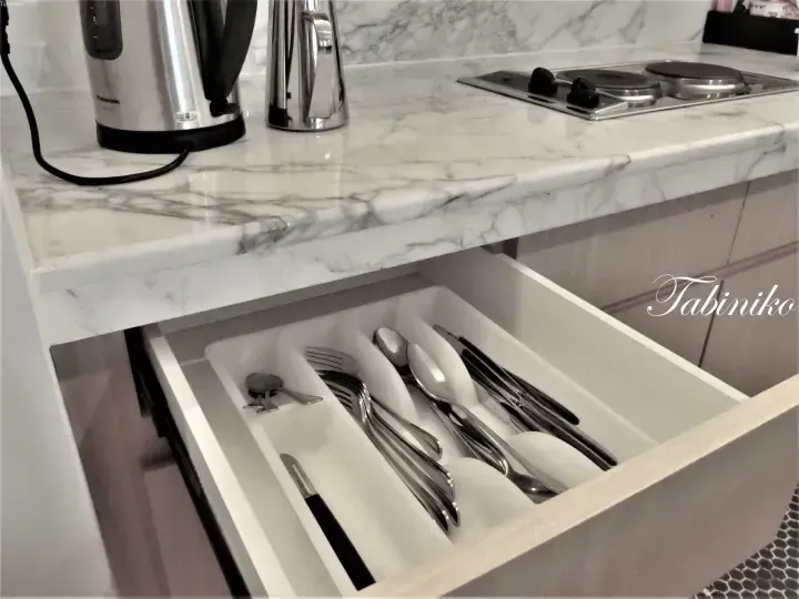 Open drawer with cutlery organizer in modern kitchen featuring marble countertop and Panasonic kettle