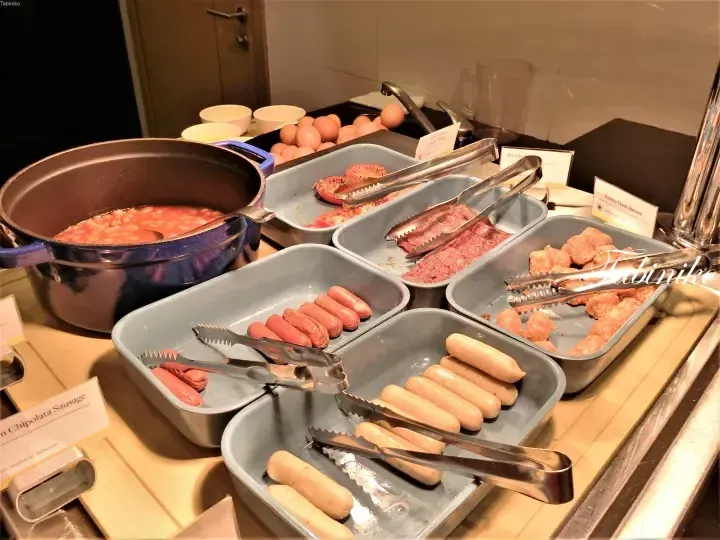 Buffet breakfast spread featuring sausages, baked beans, hash browns, and eggs at a Malaysian hotel.