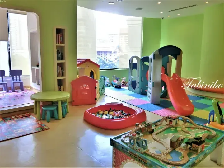 Bright children&rsquo;s playroom with colorful toys, slide, and train table in a modern apartment with city views.