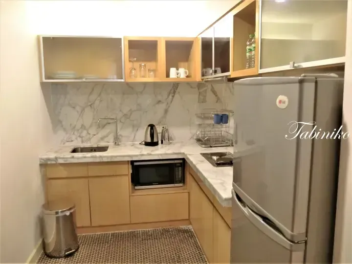 Modern kitchenette with marble countertops, wooden cabinets, LG refrigerator, and microwave in a serviced apartment.