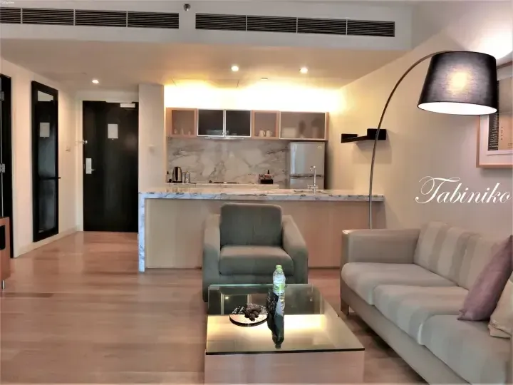 Modern serviced apartment living room with marble kitchen counter, grey armchair, and beige sofa.