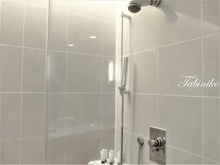 Modern shower area with light grey tiles, chrome fixtures, and toiletries in a hotel bathroom.