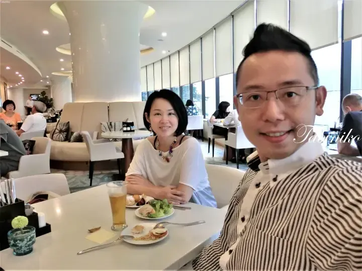A couple dining at a bright hotel lounge with buffet food and drinks on the table.