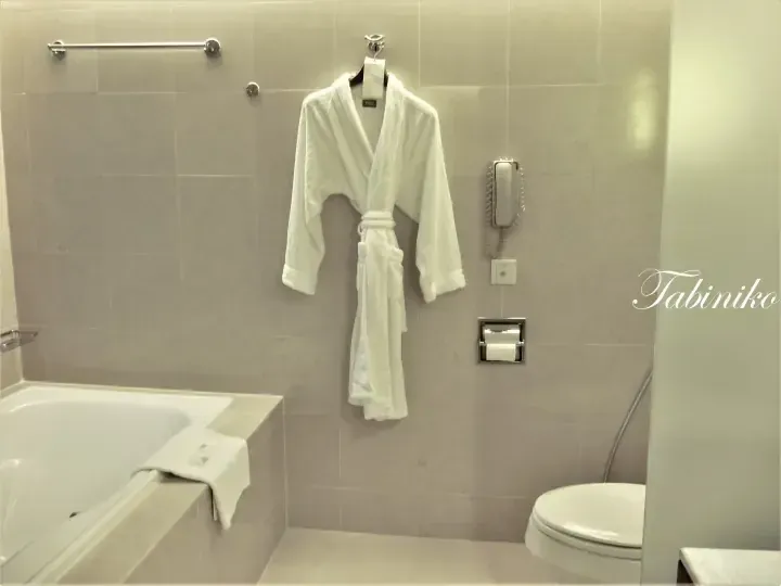White bathrobe hanging on a hook in a modern hotel bathroom with a bathtub and toilet