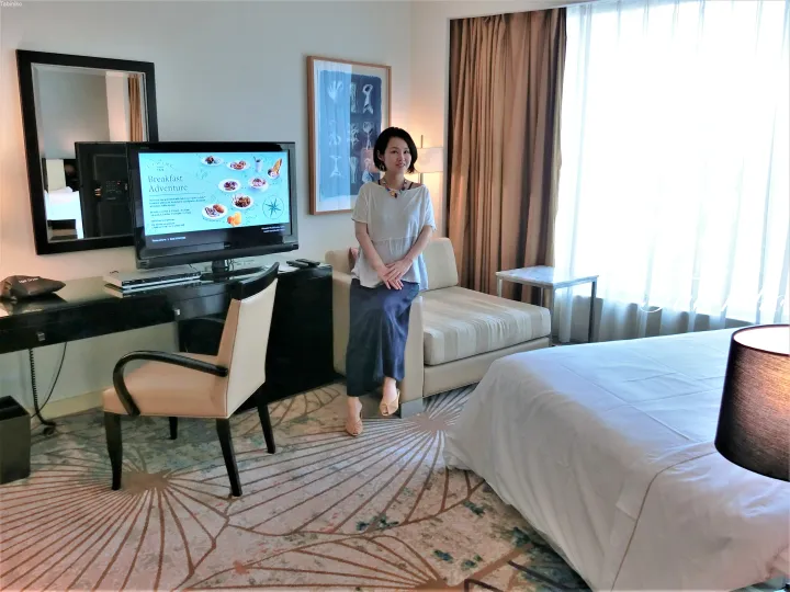 ソファと朝食メニューが表示されたテレビの前に立つ女性。