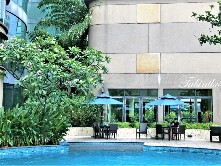 Outdoor poolside seating with blue umbrellas and lush greenery at a modern property.
