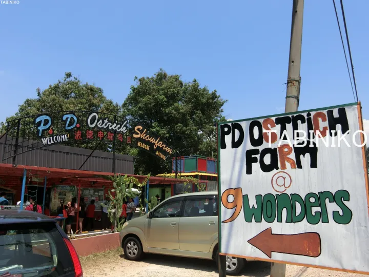マレーシアのポートディクソンにあるPD Ostrich Farm @ 9 Wondersの入口看板と訪問客、駐車中の車。