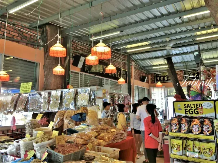 Interior of a Malaysian local market stall displaying packaged snacks, dried seafood, and salted egg products under traditional red lanterns.