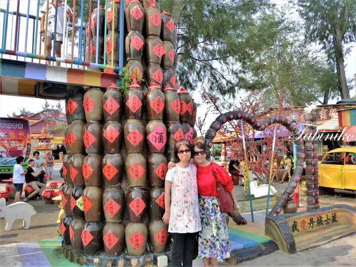 中国語の文字が書かれた大きな陶器の壺が積み上げられた展示の前でポーズをとる二人の女性。