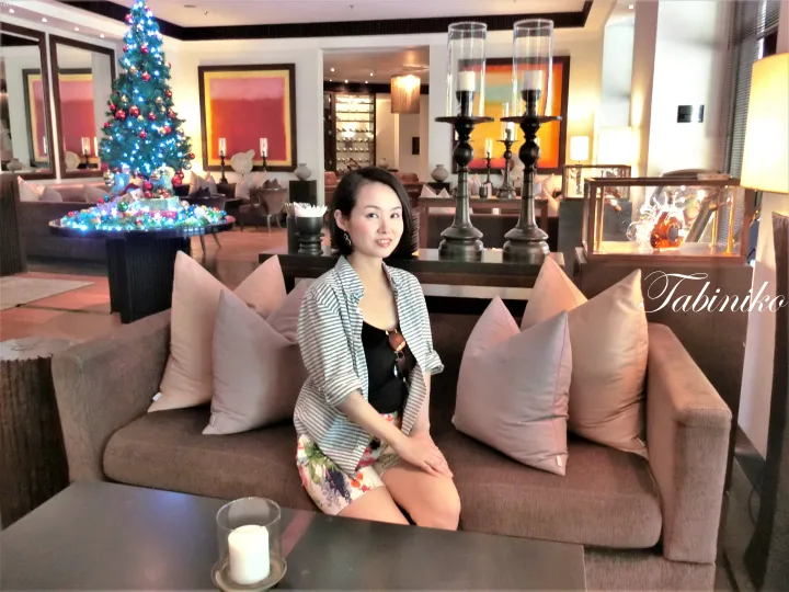 クリスマスツリーとキャンドルスタンドのあるホテルロビーでソファに座る女性。