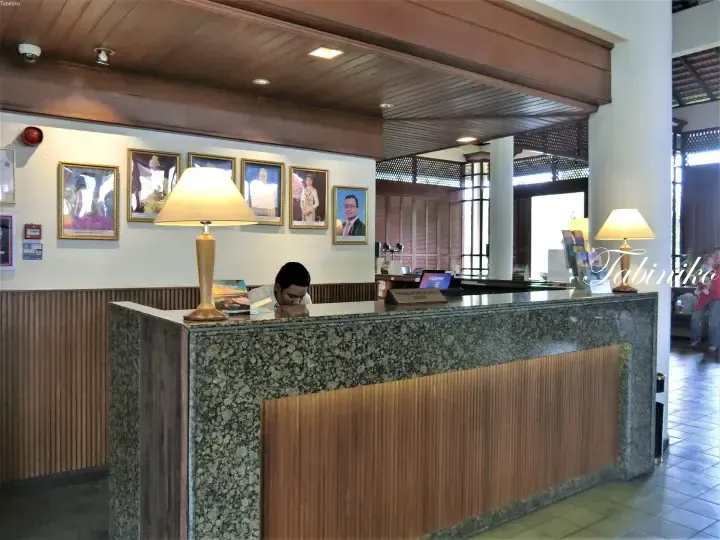 Reception desk at a Malaysian hotel lobby with granite counter, wooden accents, and framed portraits on the wall.