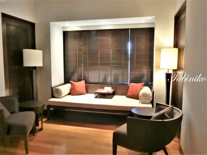 Modern hotel lounge with a window seat, orange cushions, and floor lamps in a contemporary room.